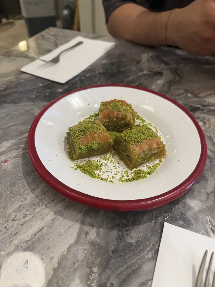 Three pieces of baklava topped with ground pistachio on a red-rimmed plate